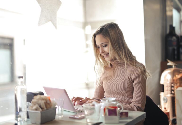 Woman sitting in coffee shop, smiling at her laptop while looking at eCommerce website.