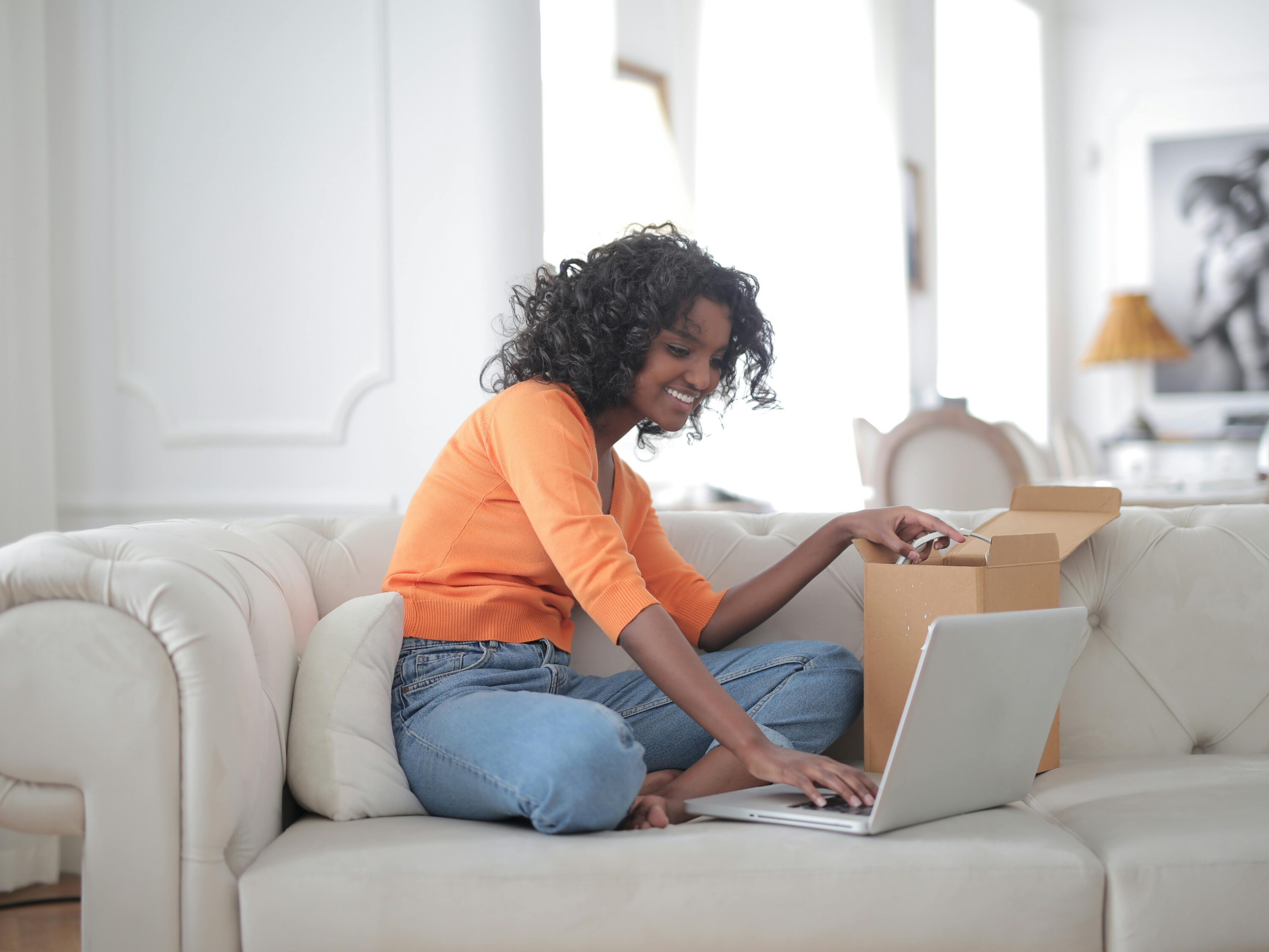 Woman sitting on couch, scrolling on laptop and smiling, looking at website.