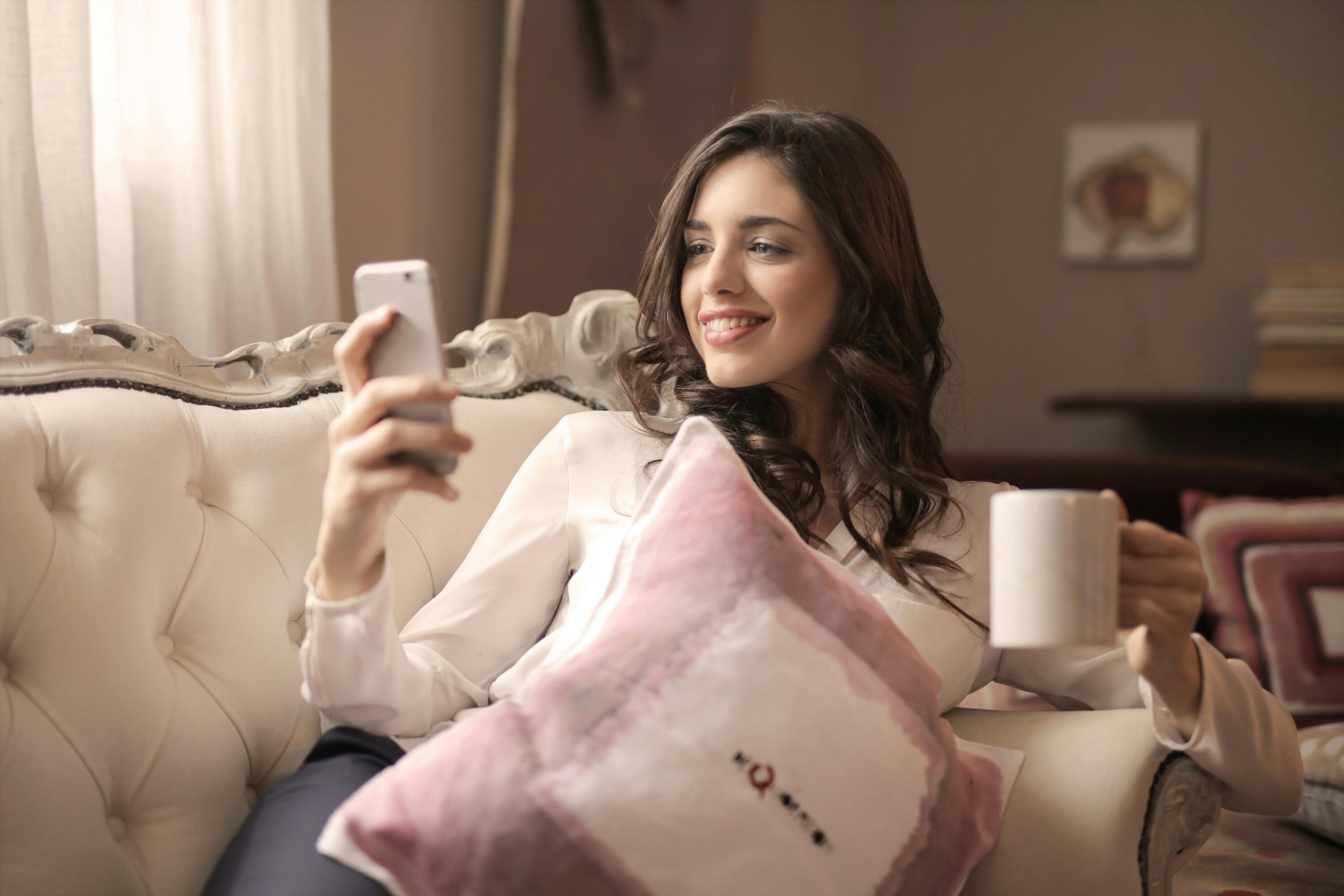 Woman laying on couch, smiling looking at her phone.