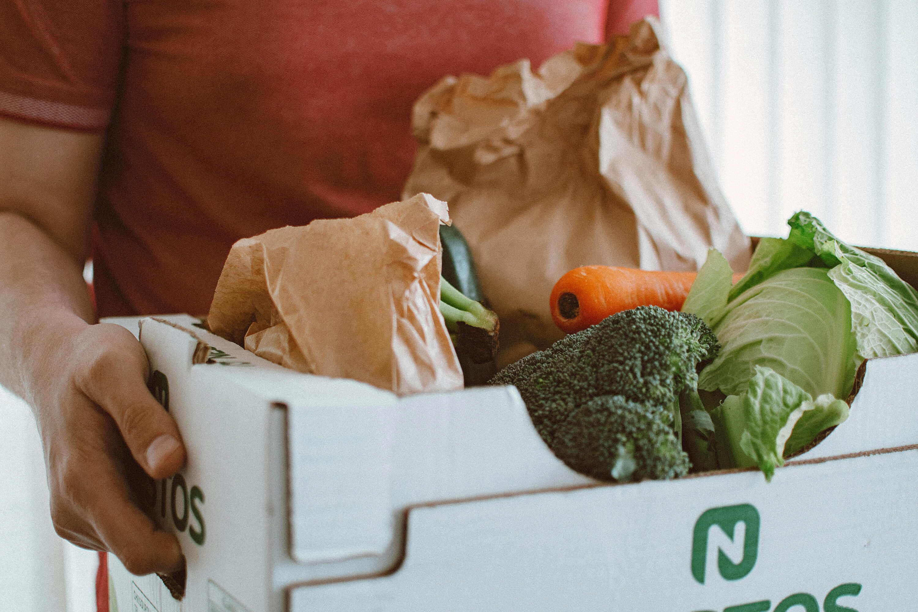 Delivery staff member holding box filled with vegetables.