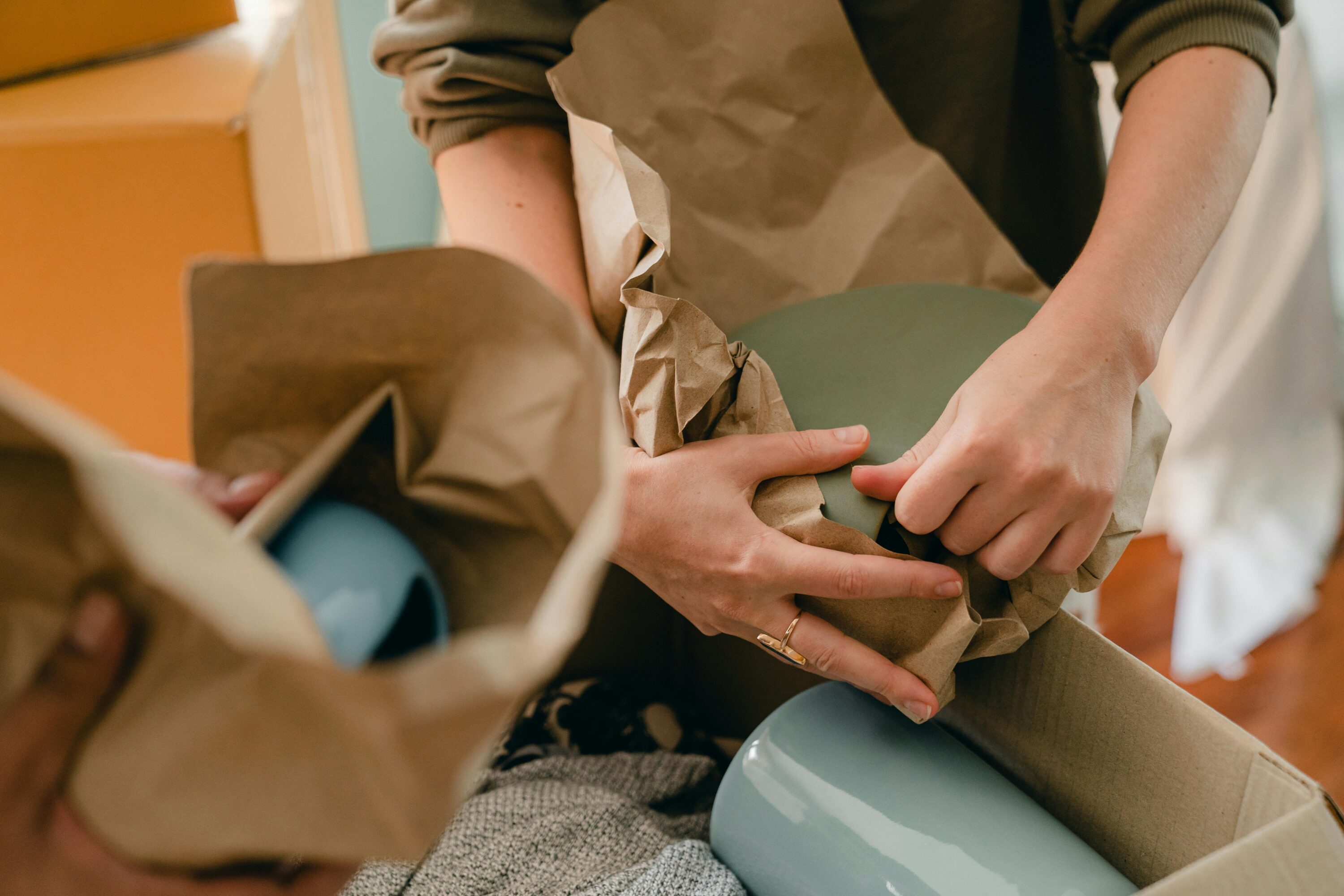 People wrapping ceramic plates in brown paper.