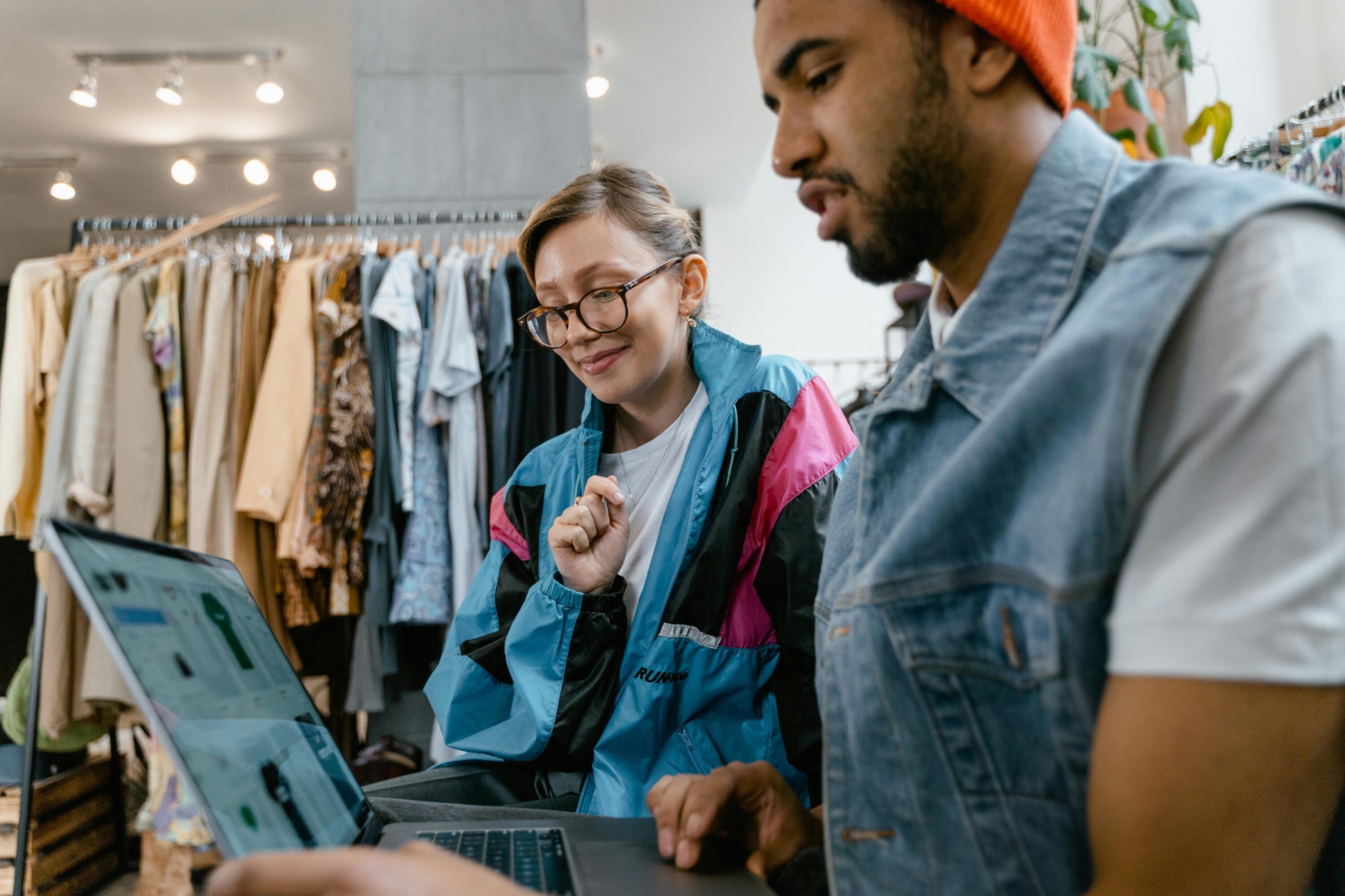 Woman and man sitting in a clothing shop, both looking on a laptop at their ecommerce fashion industry website.