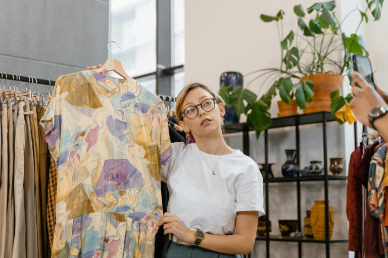 Woman holding up a dress in a clothing shop, with a man taking a photo, for the second-hand eCommerce fashion industry.